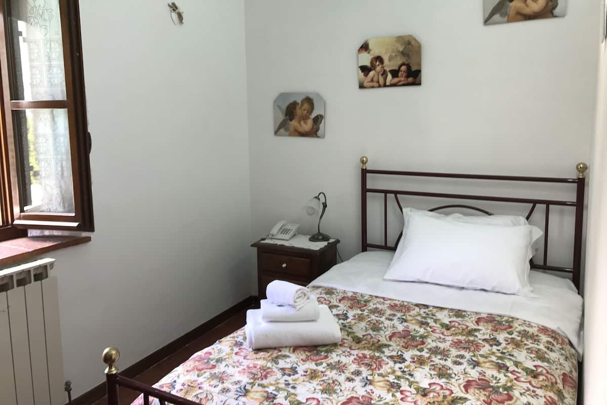 Une chambre à coucher avec un lit en bois, du linge de lit blanc, une table de chevet avec une lampe et des œuvres d’art accrochées au mur.