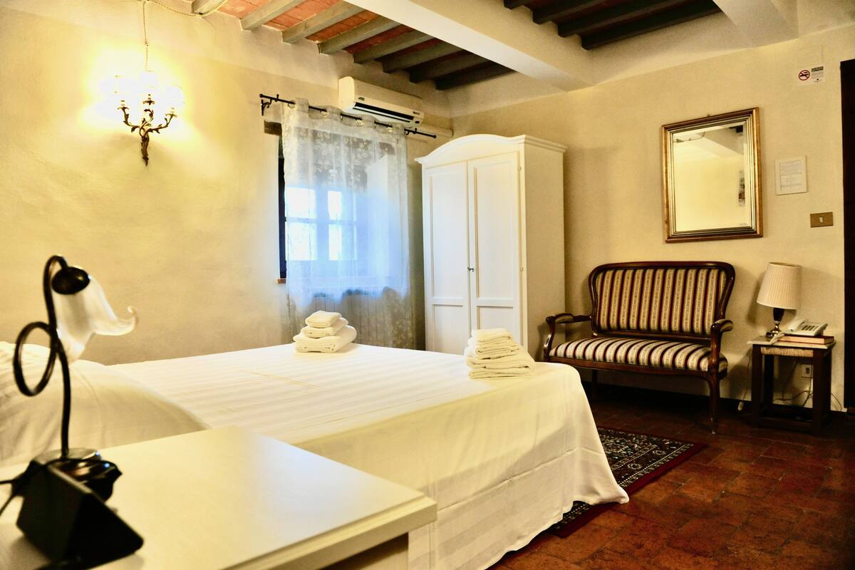 Une chambre d’hôtel comprenant un lit, une chaise, une armoire, un miroir et un bureau avec une lampe.