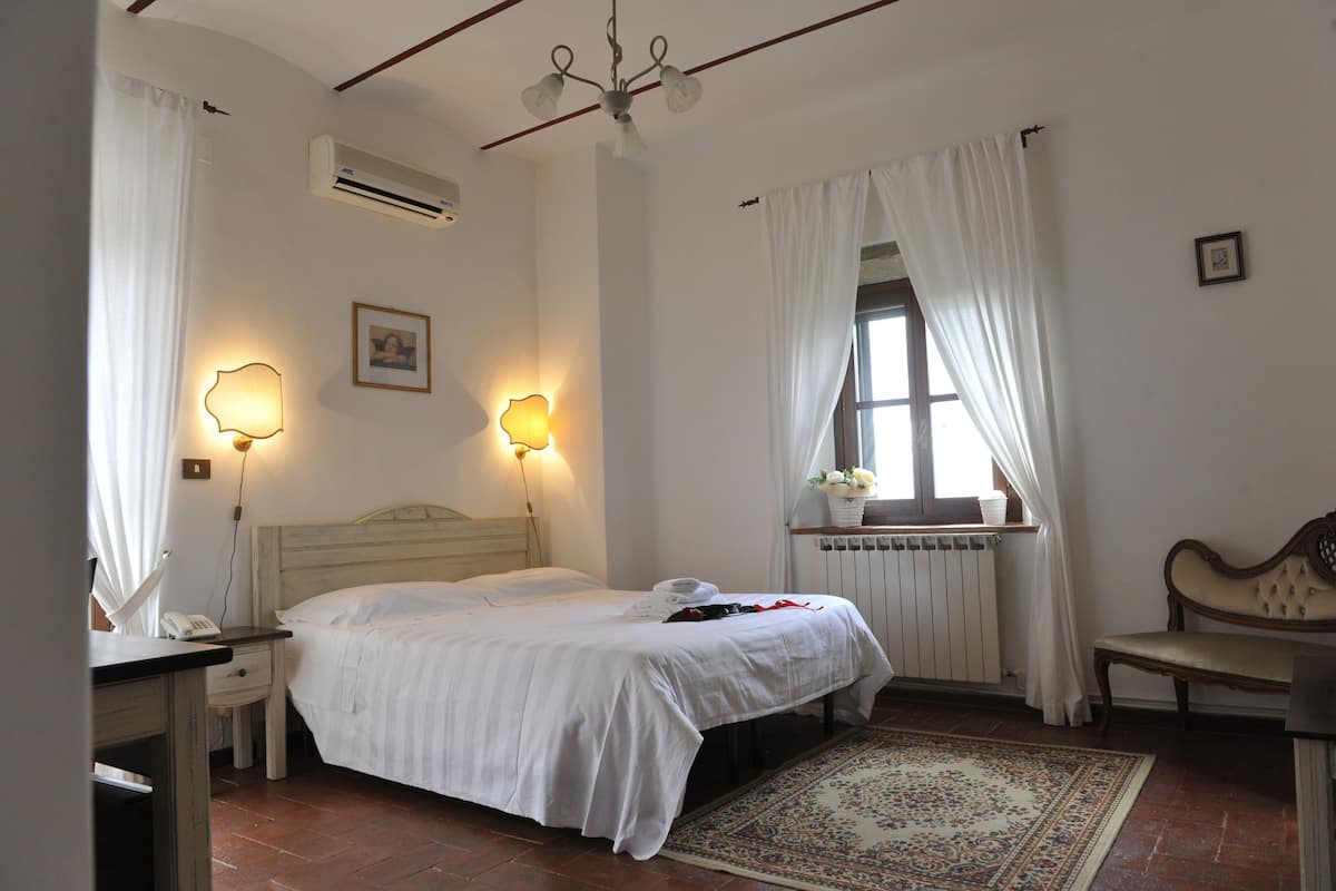 Une chambre à coucher avec un lit, des lampes de chevet, un radiateur, un banc et une fenêtre avec des rideaux.