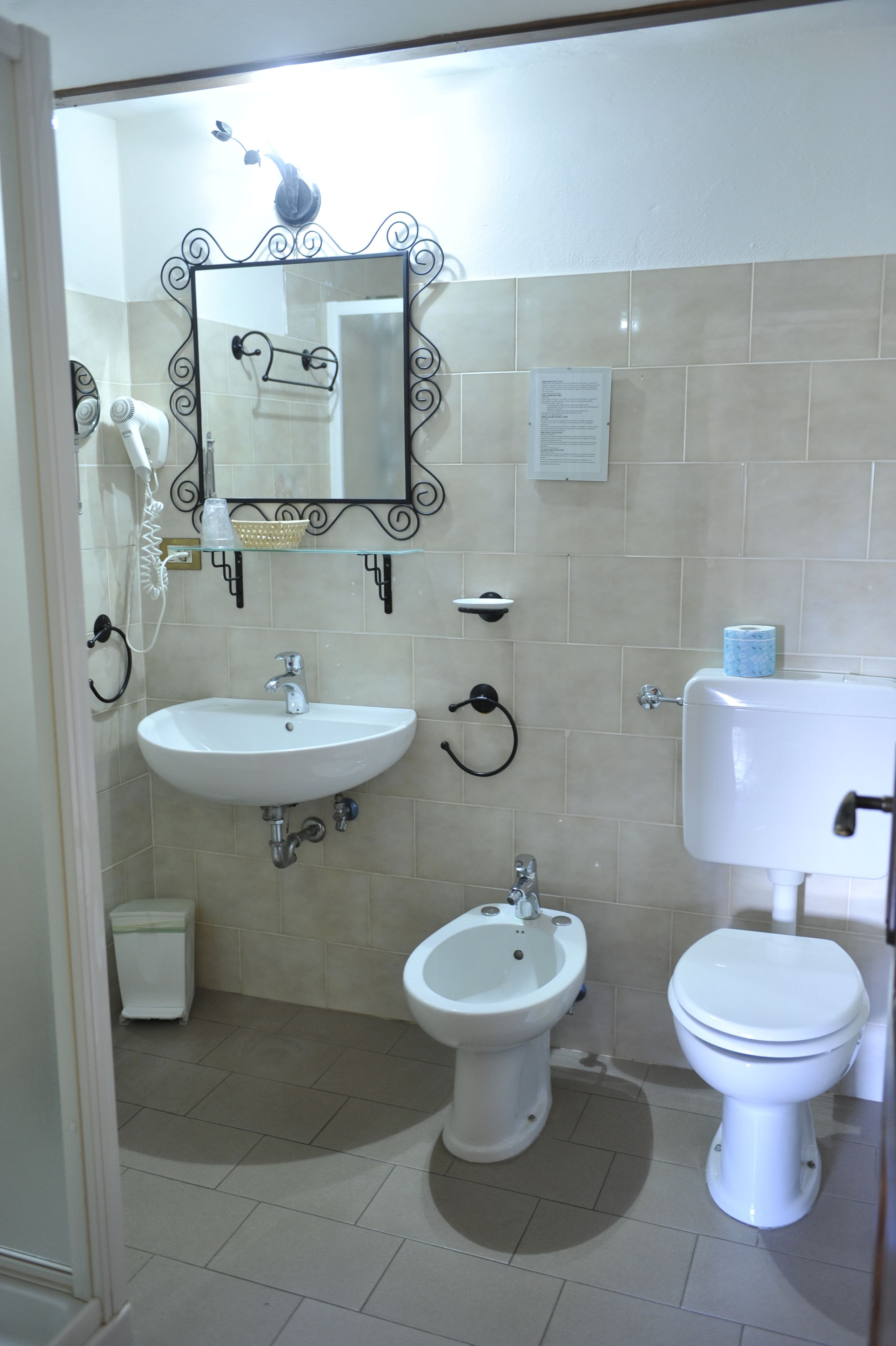 A bathroom with a white sink, bidet, toilet, and a mirror with decorative frame.