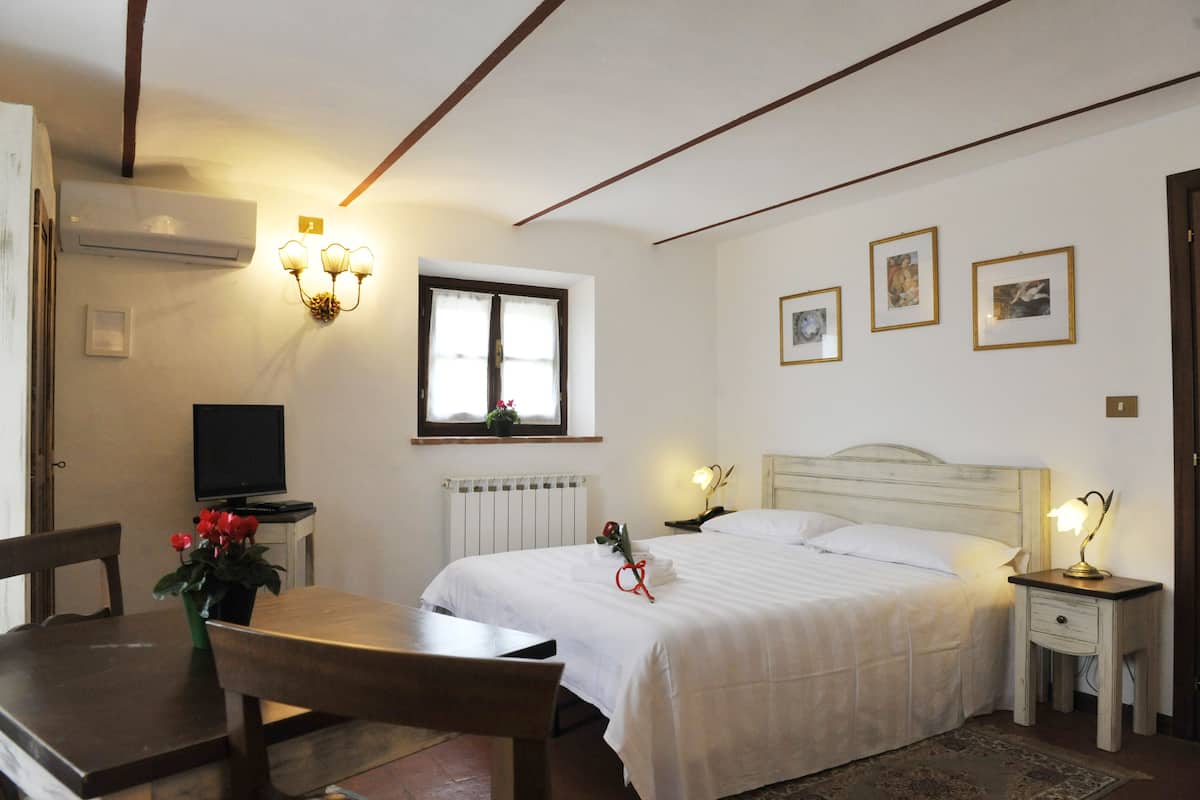 Une chambre à coucher avec un lit, des tables de chevet, un bureau et une chaise. Il y a une fenêtre avec des rideaux, un radiateur et des lampes fixées au mur.