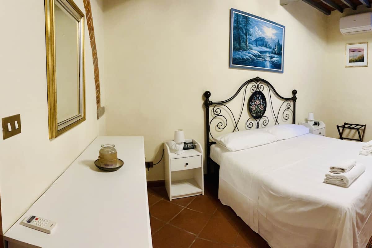 Une chambre à coucher comprenant un lit, une table de chevet, une commode, un canapé blanc, un tapis à motifs et une porte donnant sur une autre pièce.