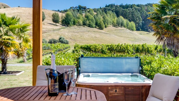 Un jacuzzi con una mesa de madera y dos copas de vino, rodeado de exuberante follaje y colinas.