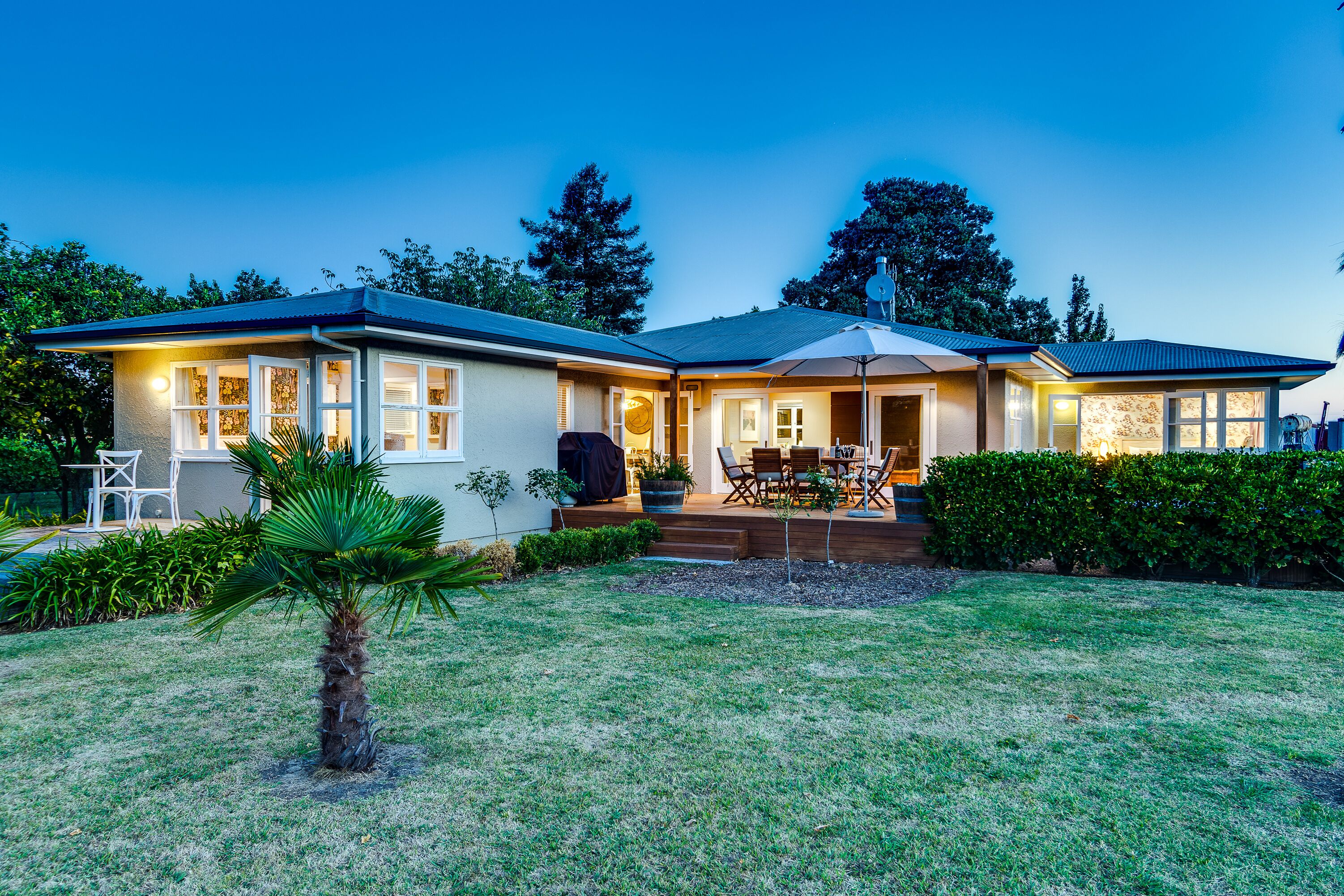 A two-story house with a well-maintained lawn, outdoor seating area, and a large umbrella.