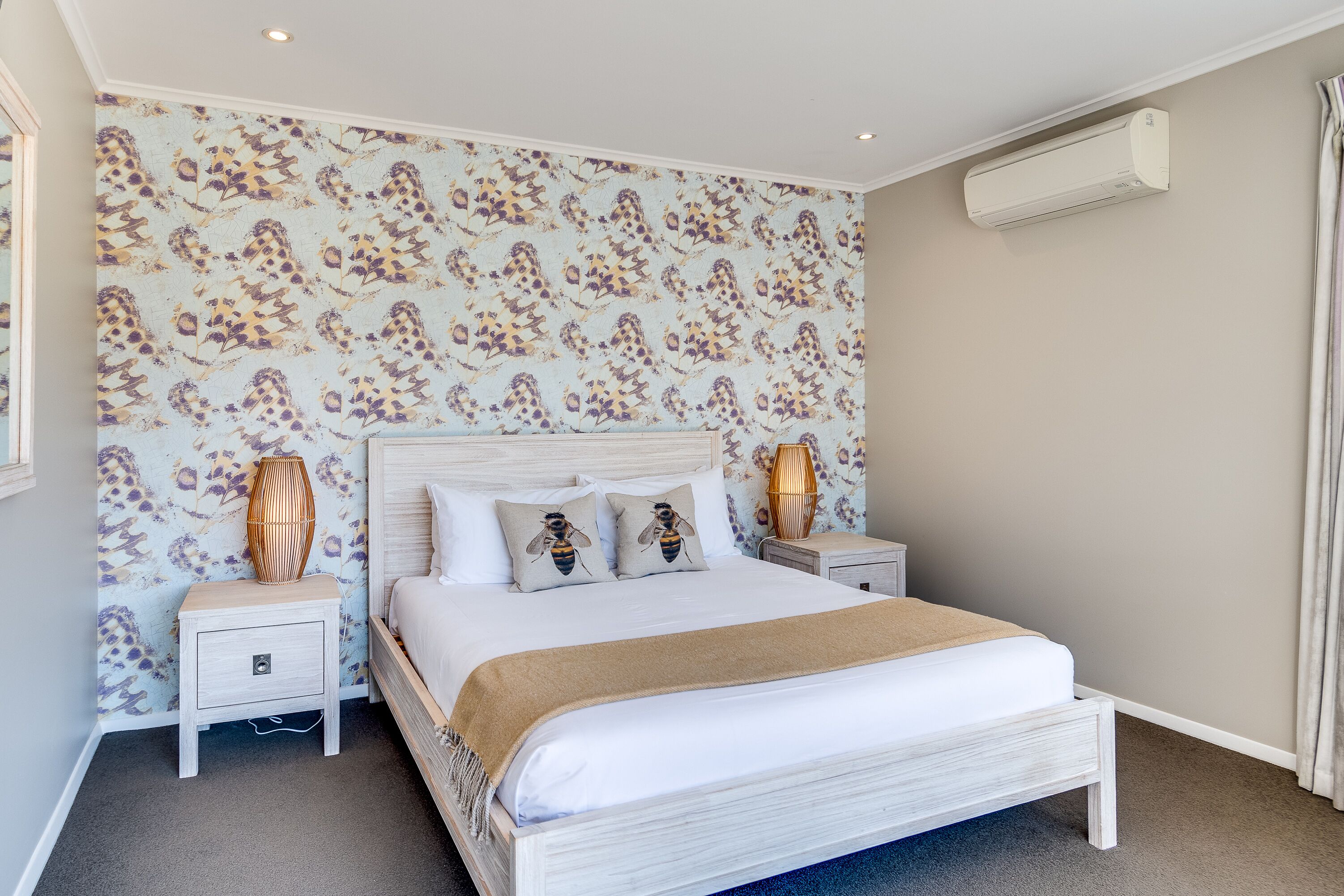A bedroom with a bed, nightstands, a wall-mounted air conditioner, and a patterned wallpaper.