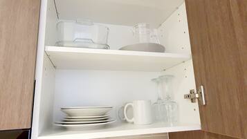 Een keukenkastje met planken waarop drinkglazen, borden en een kan staan.