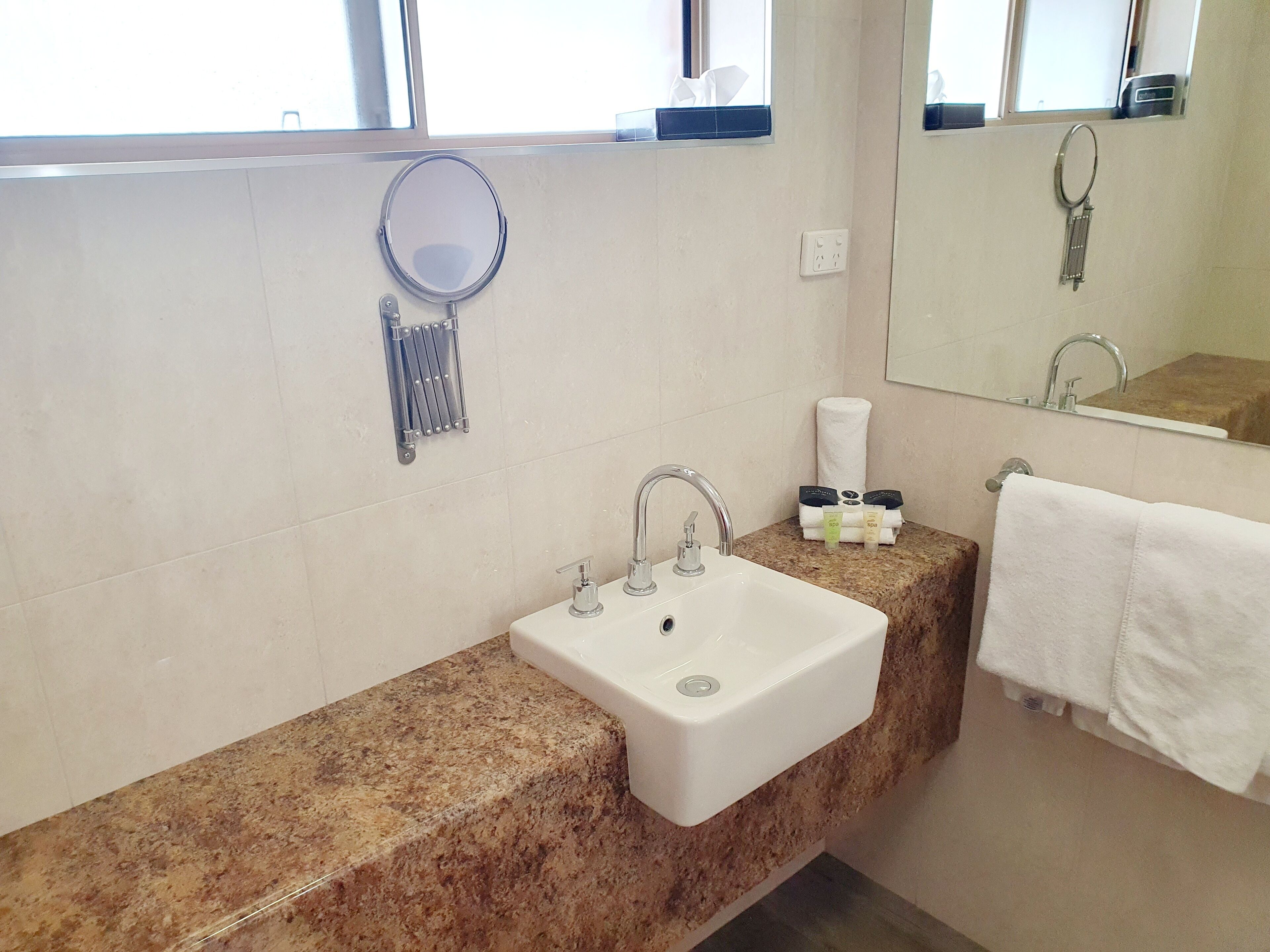A bathroom with a white sink, two faucets, a mirror, and a towel rack.