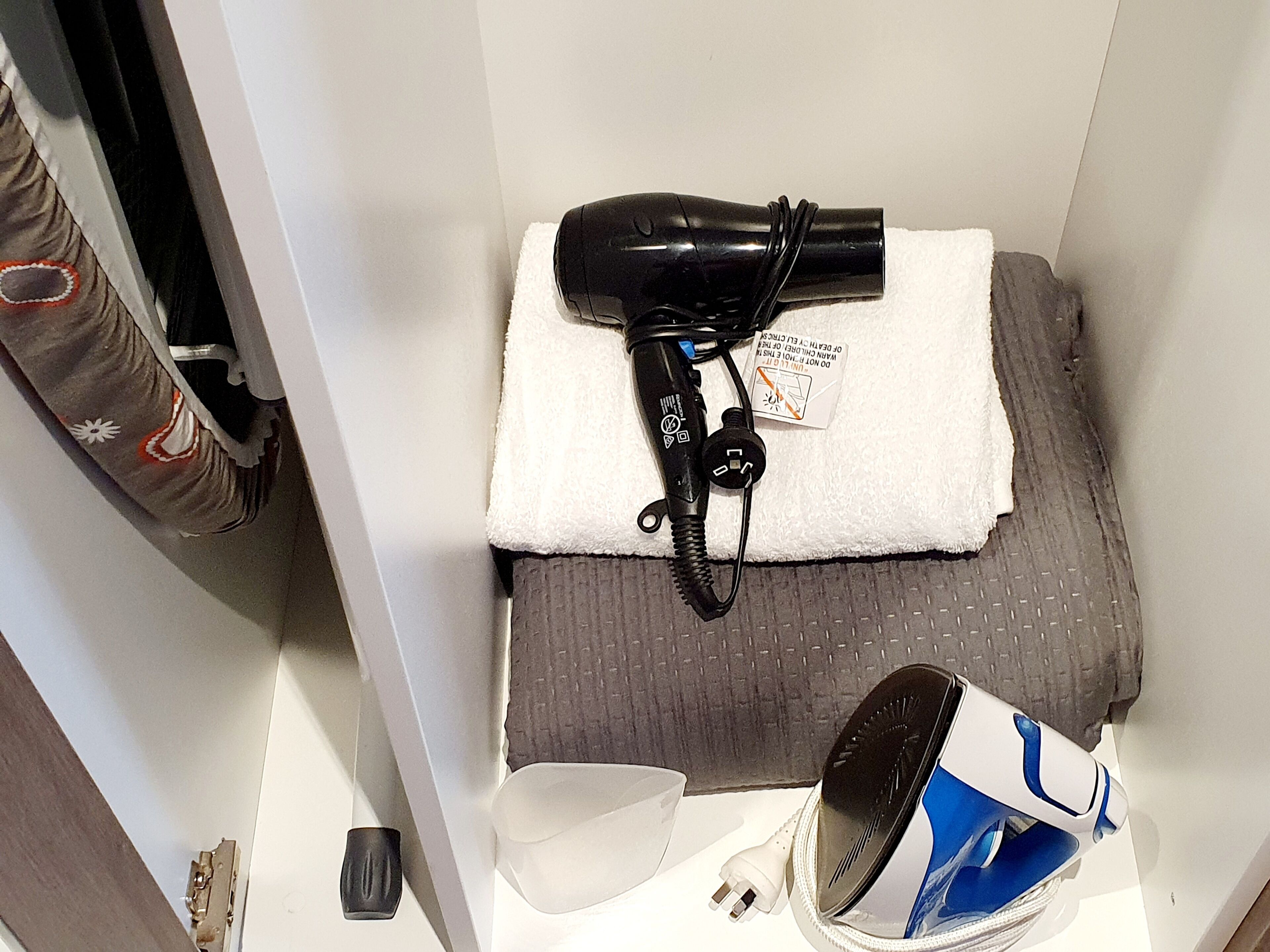 A small hotel room with a hairdryer, a towel, and a mirror on a shelf.
