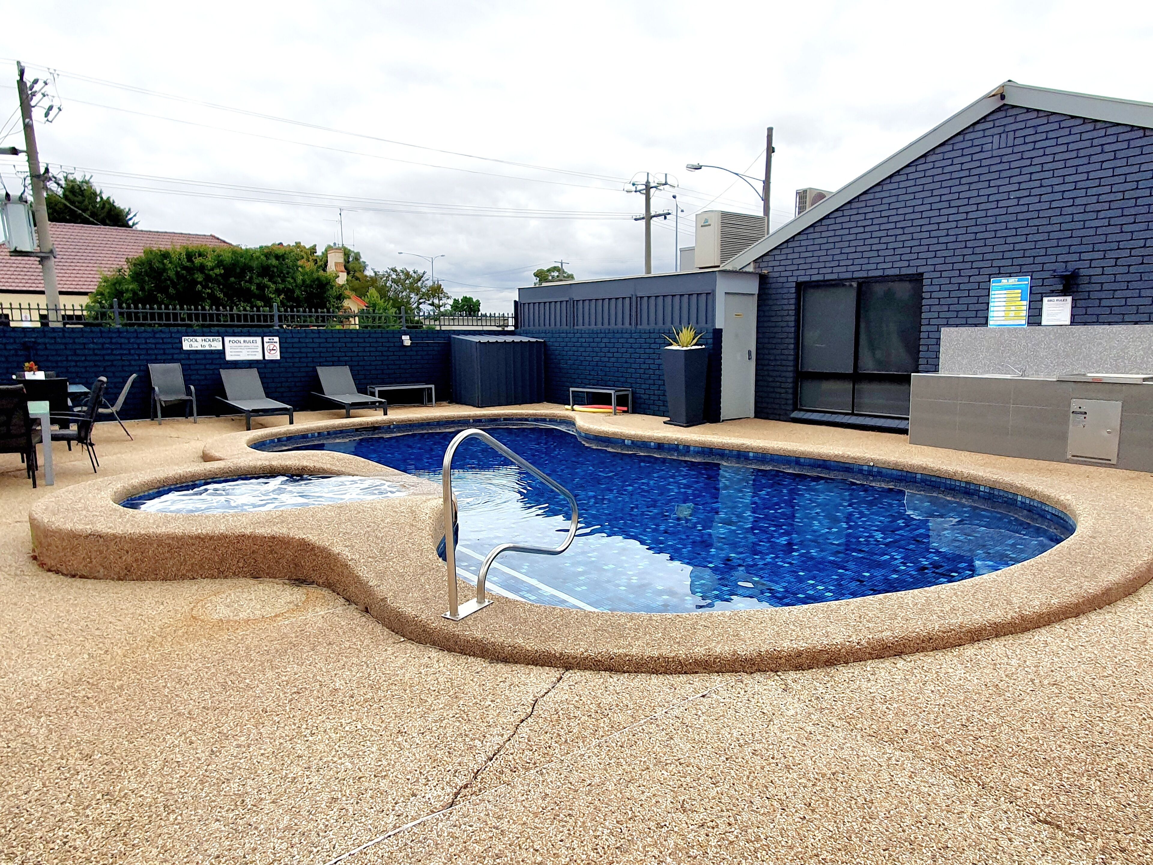 A swimming pool with a unique shape, surrounded by lounge chairs and a brick wall.