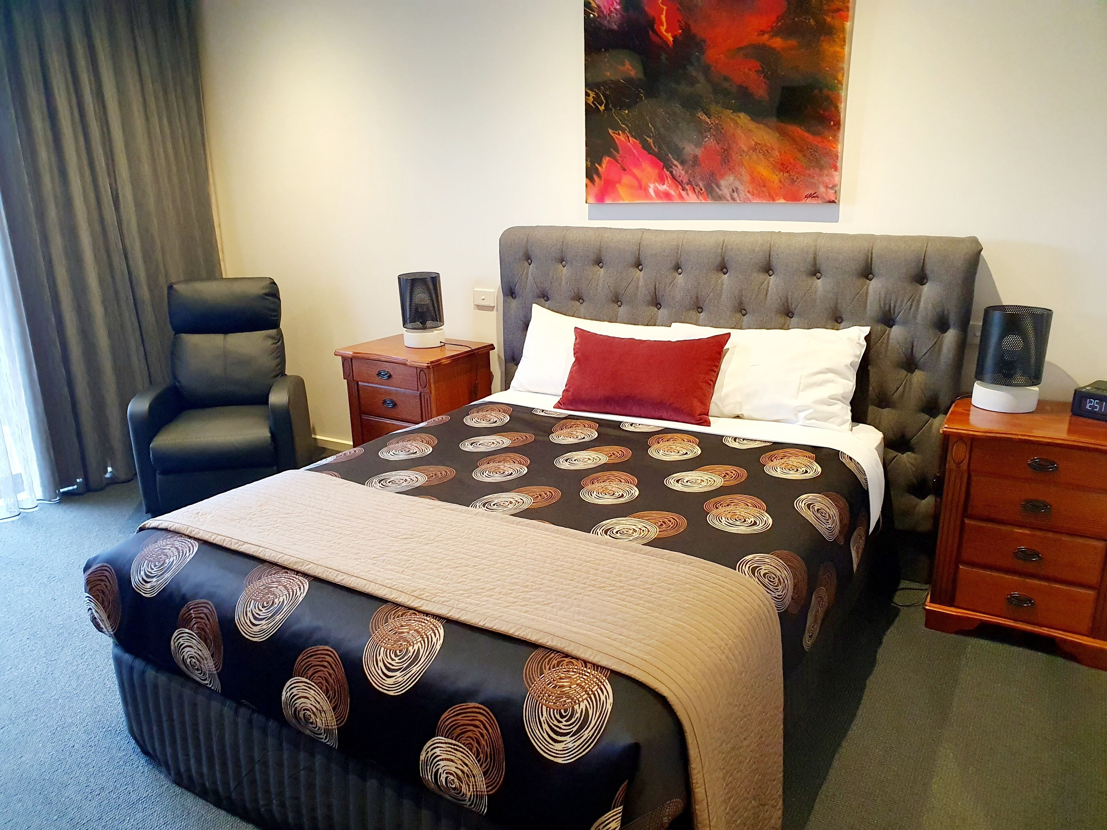 A hotel room with a large bed, a chair, a nightstand, and a painting on the wall.