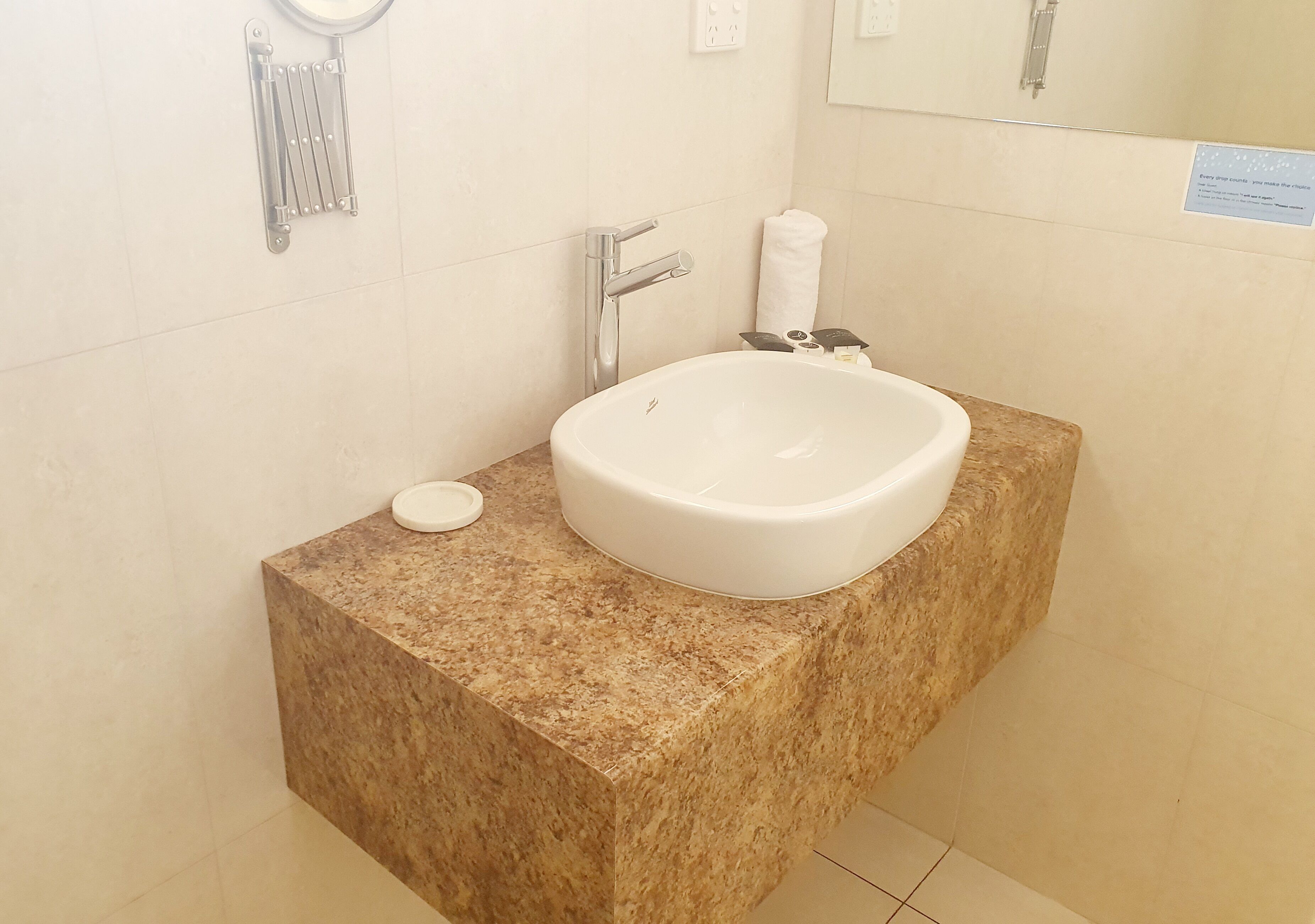 A bathroom with a white sink, a towel dispenser, and a mirror.