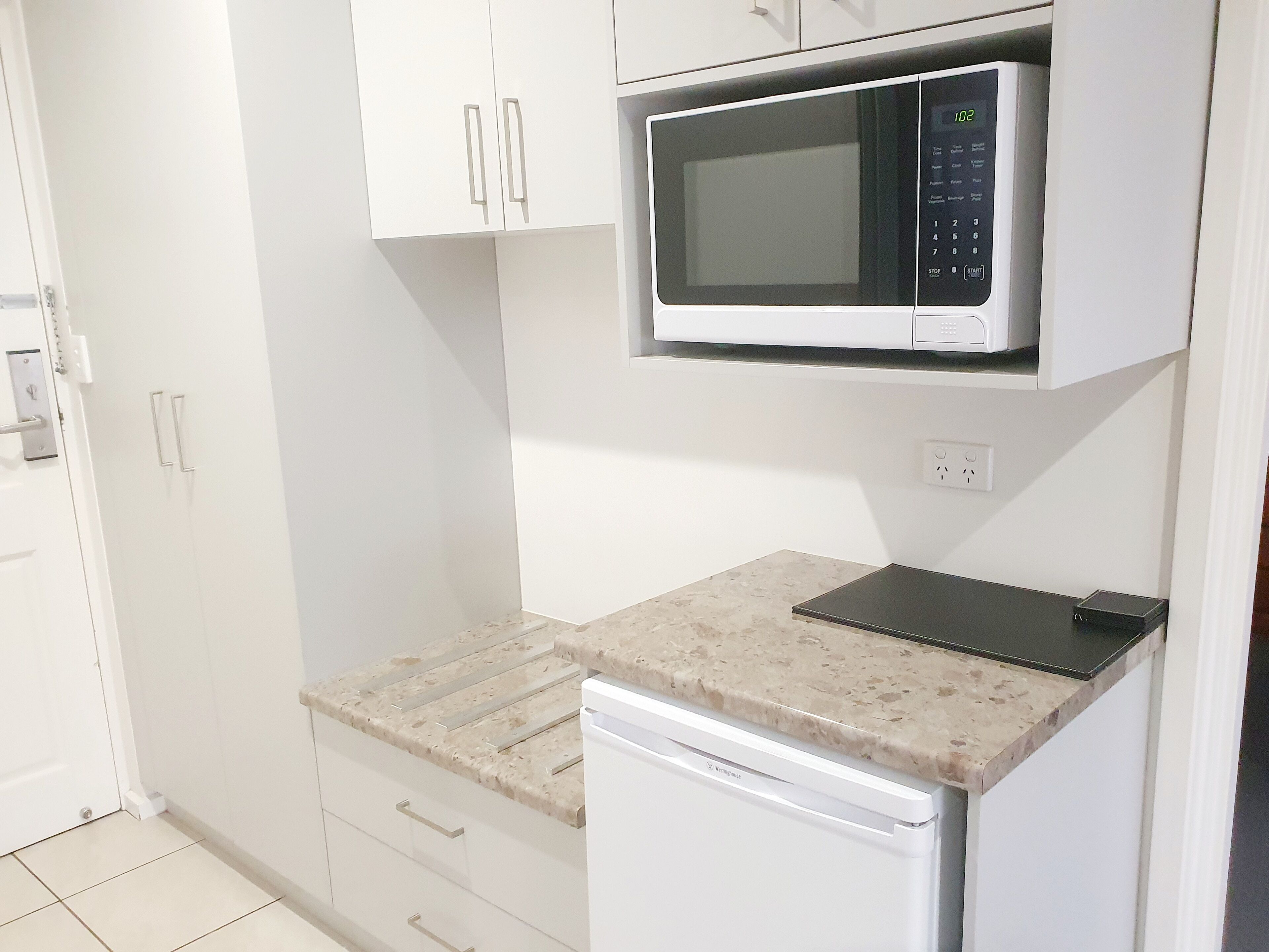 A compact kitchen with white cabinets, a microwave, a dishwasher, and a granite countertop.