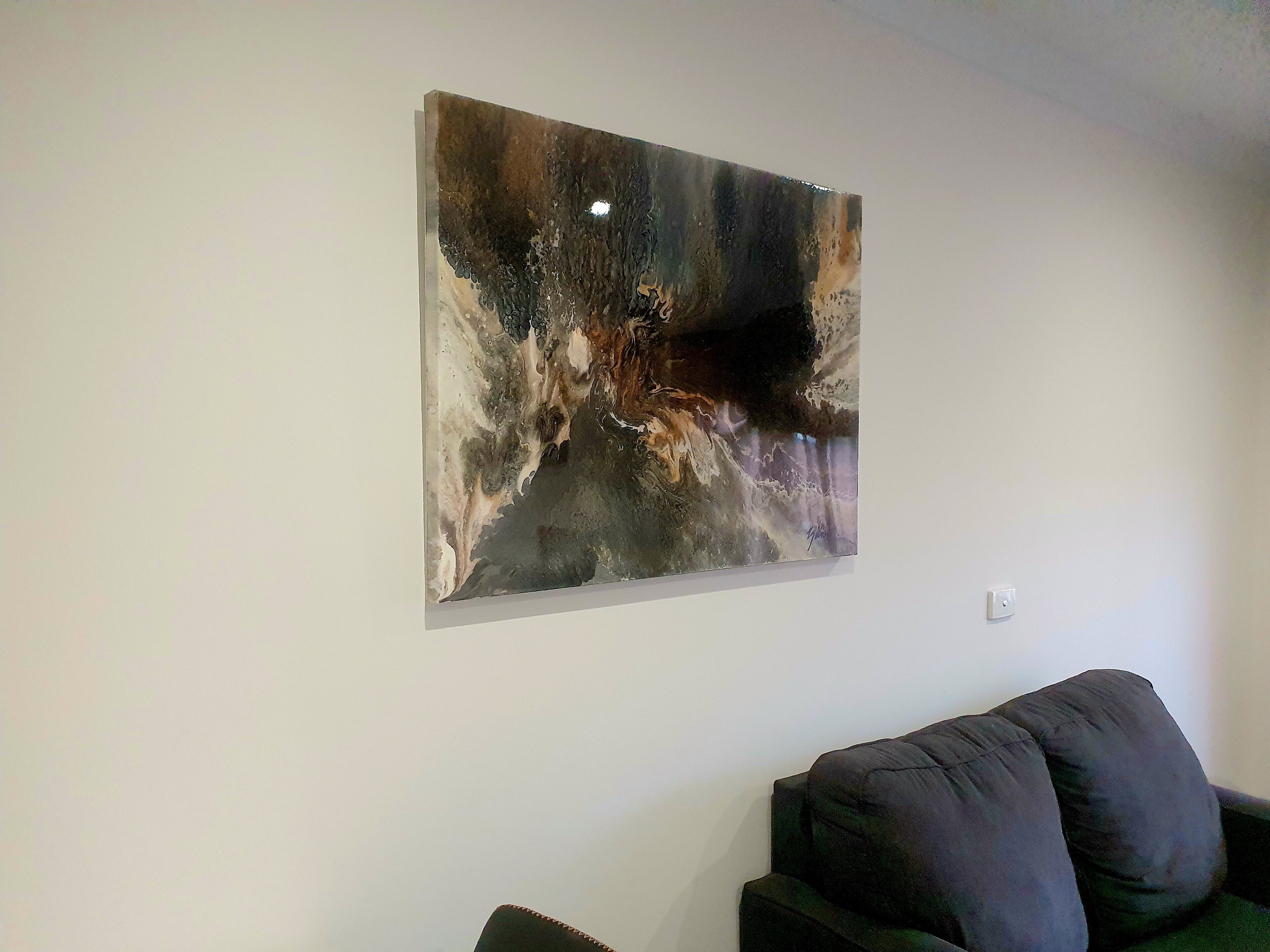 A modern living room with a large abstract painting on the wall, a dark-colored sofa, and a white wall.