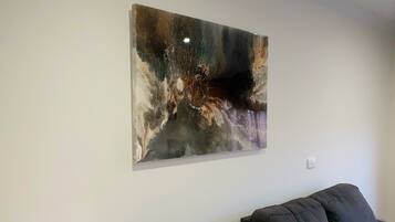 A modern living room with a large abstract painting on the wall, a dark-colored sofa, and a white wall.