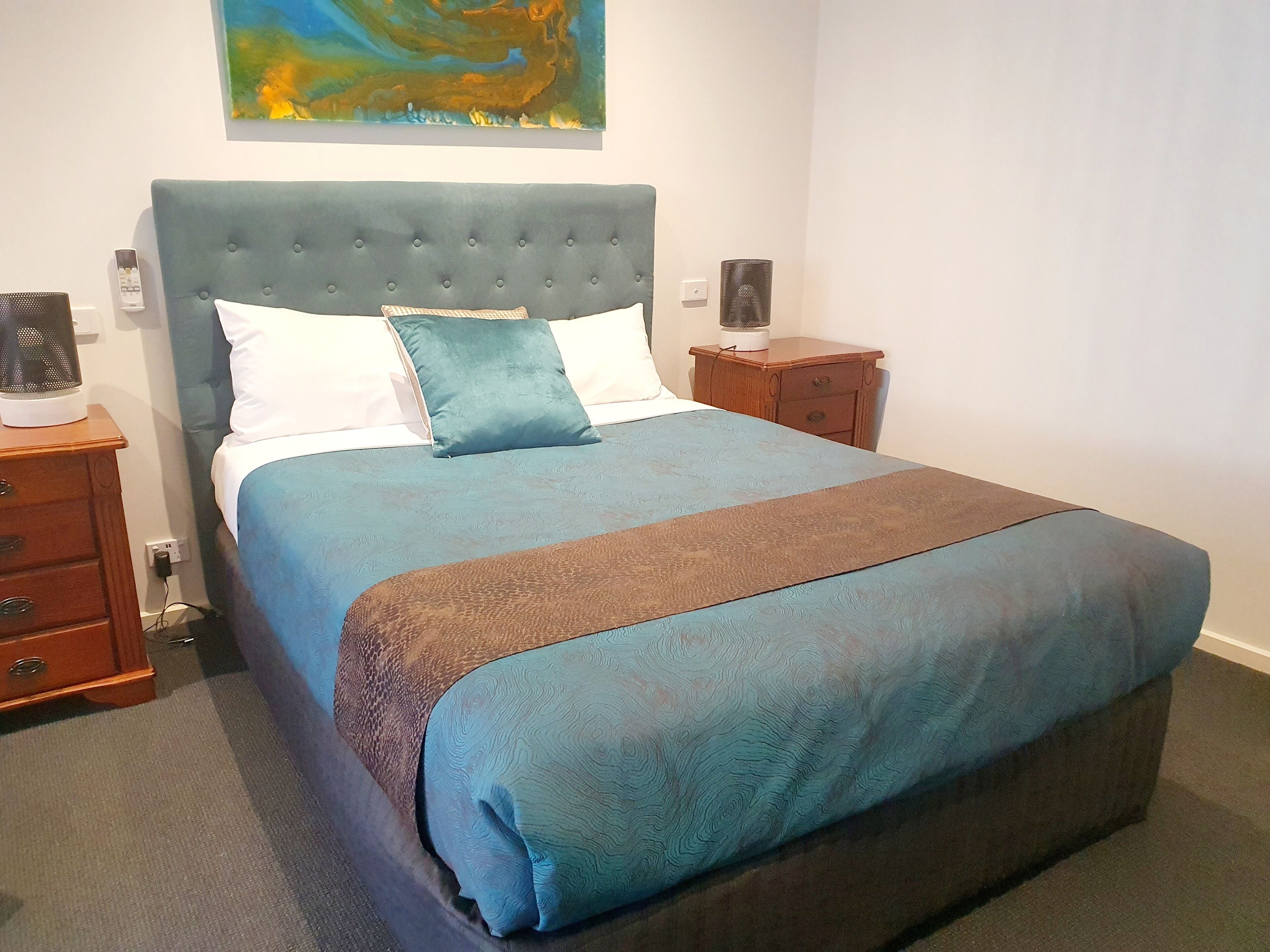 A neatly made bed with a blue and brown bedspread, a tufted headboard, and two bedside tables with lamps.