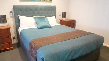 A neatly made bed with a blue and brown bedspread, a tufted headboard, and two bedside tables with lamps.