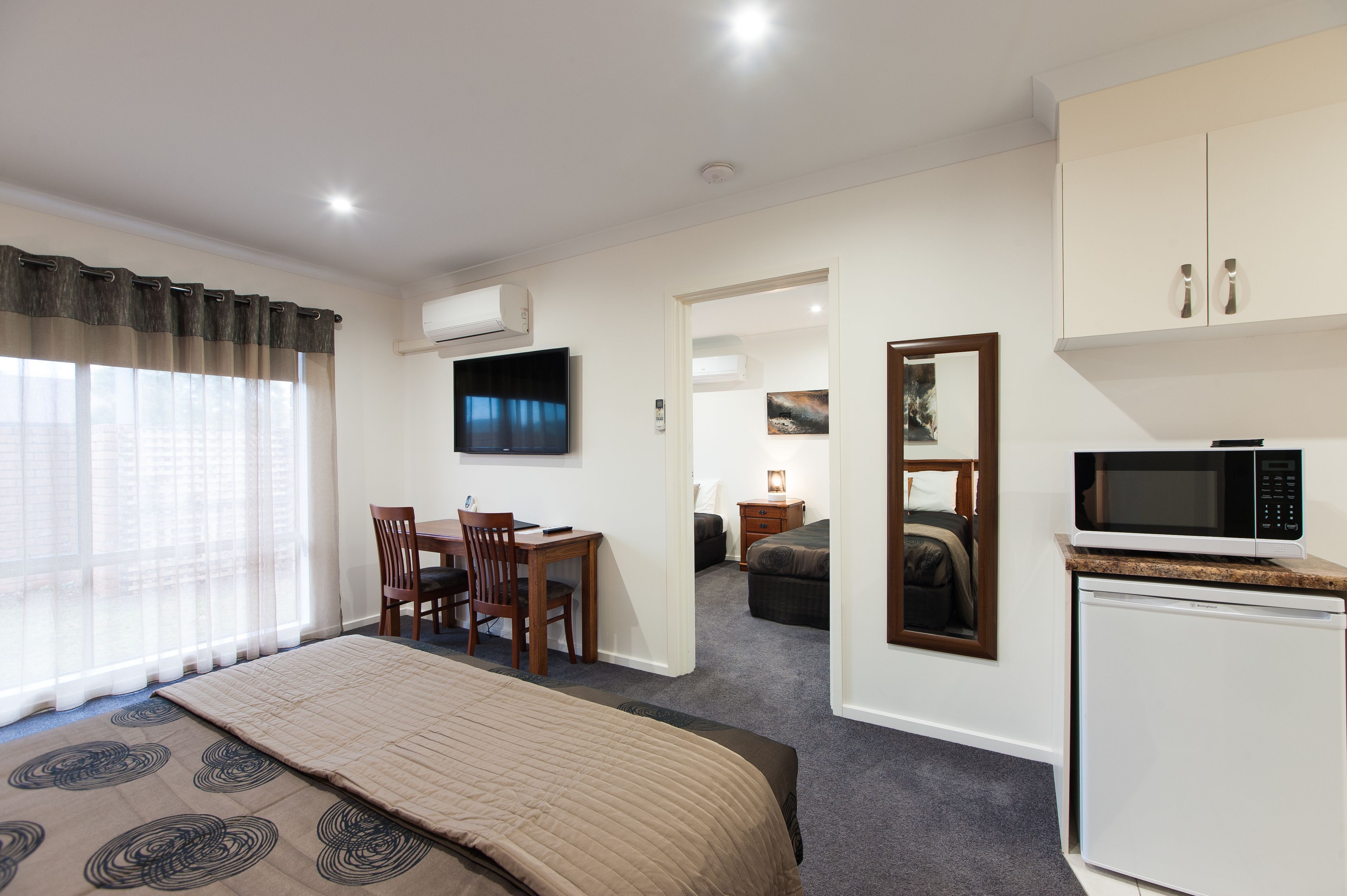 A hotel room with a bed, a desk, a chair, a television, a microwave, and a small refrigerator.