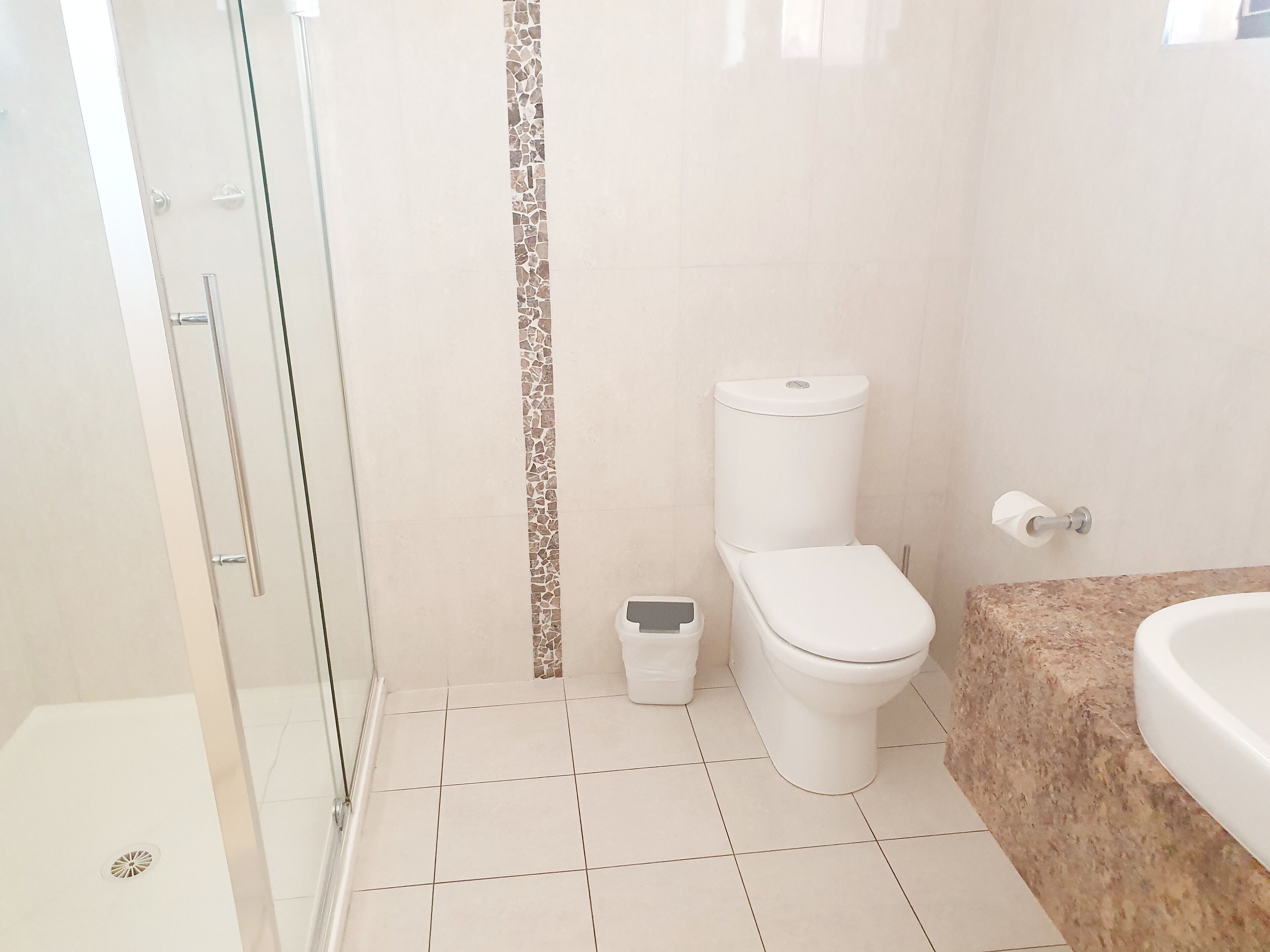 A bathroom with a glass shower enclosure, a toilet, and a sink.