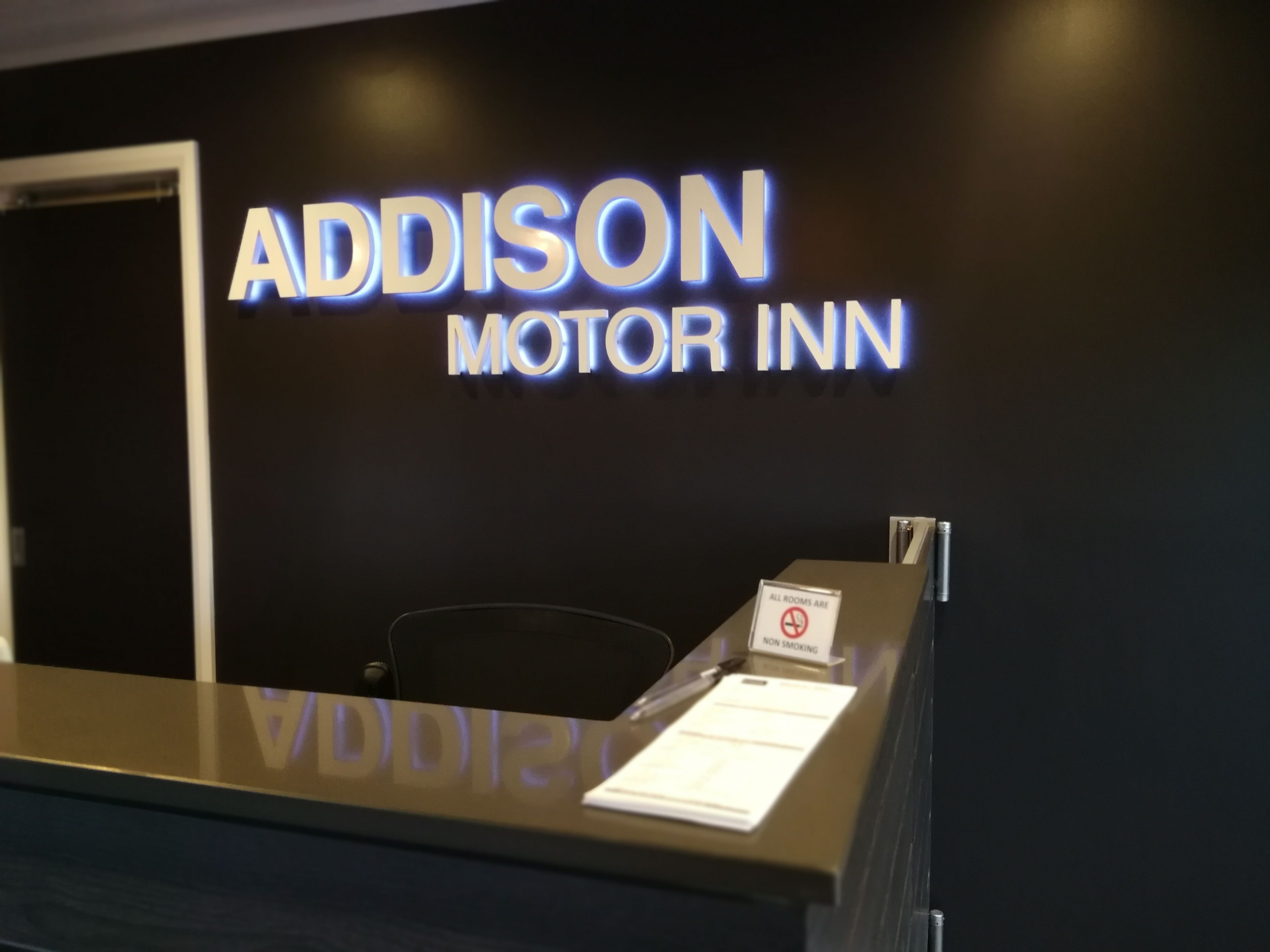A reception desk with a sign that reads "Addison Motor Inn" and a non-smoking sign.
