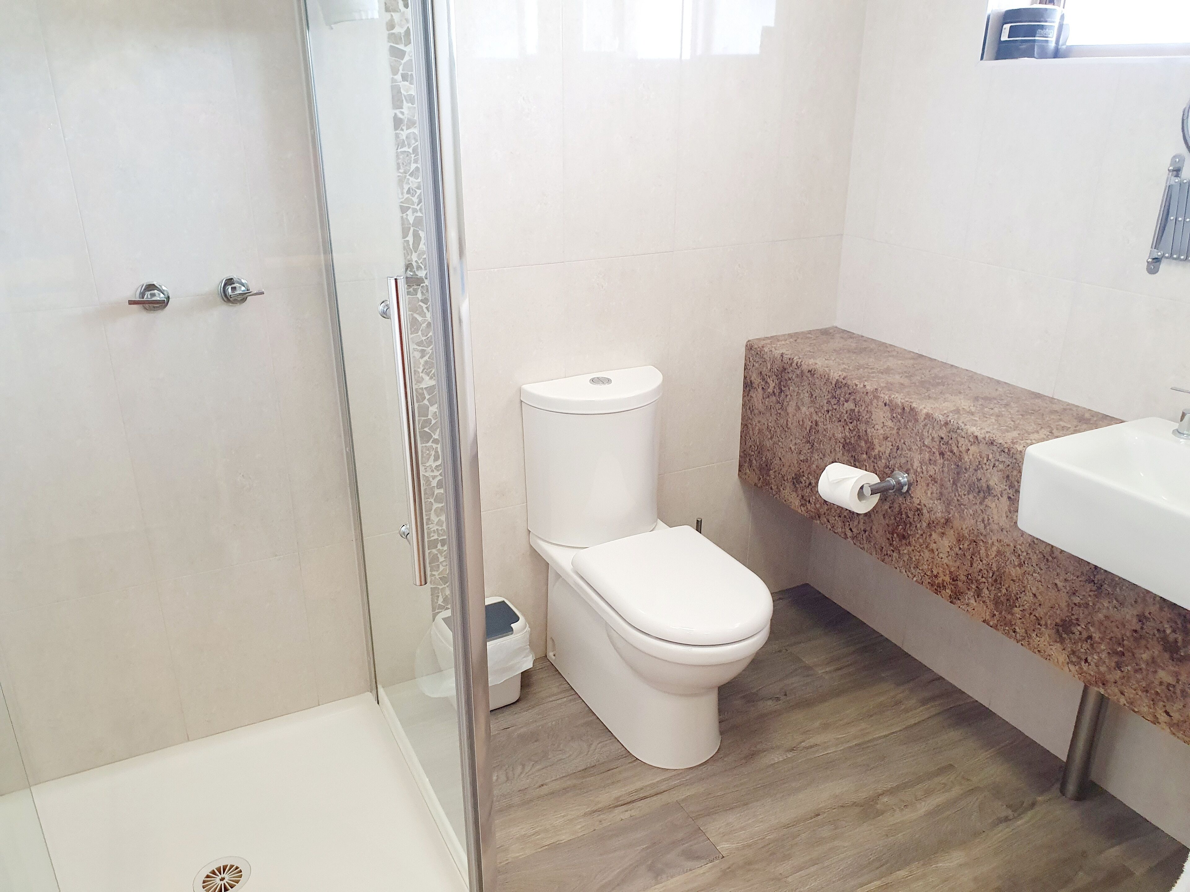 Une salle de bain avec une douche à parois de verre, des toilettes blanches, un comptoir en marbre et un lavabo.
