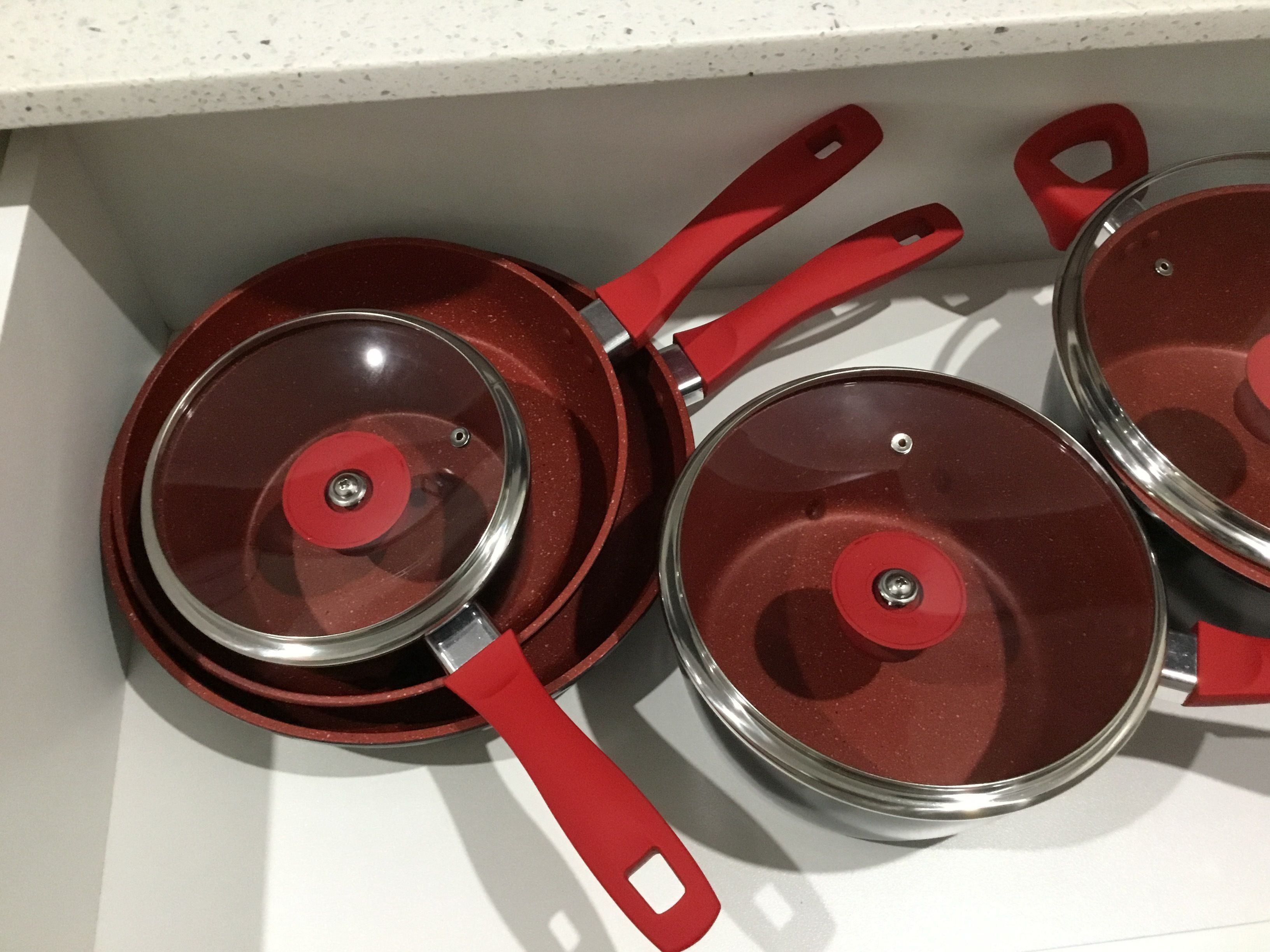 A drawer containing three red pots with lids.