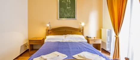 Una cama bien hecha con una colcha azul y almohadas blancas, una mesita de noche con una lámpara y un cuadro en la pared.