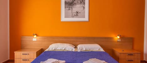 A bedroom with a bed, two bedside tables, a nightstand, and a framed picture on the wall.
