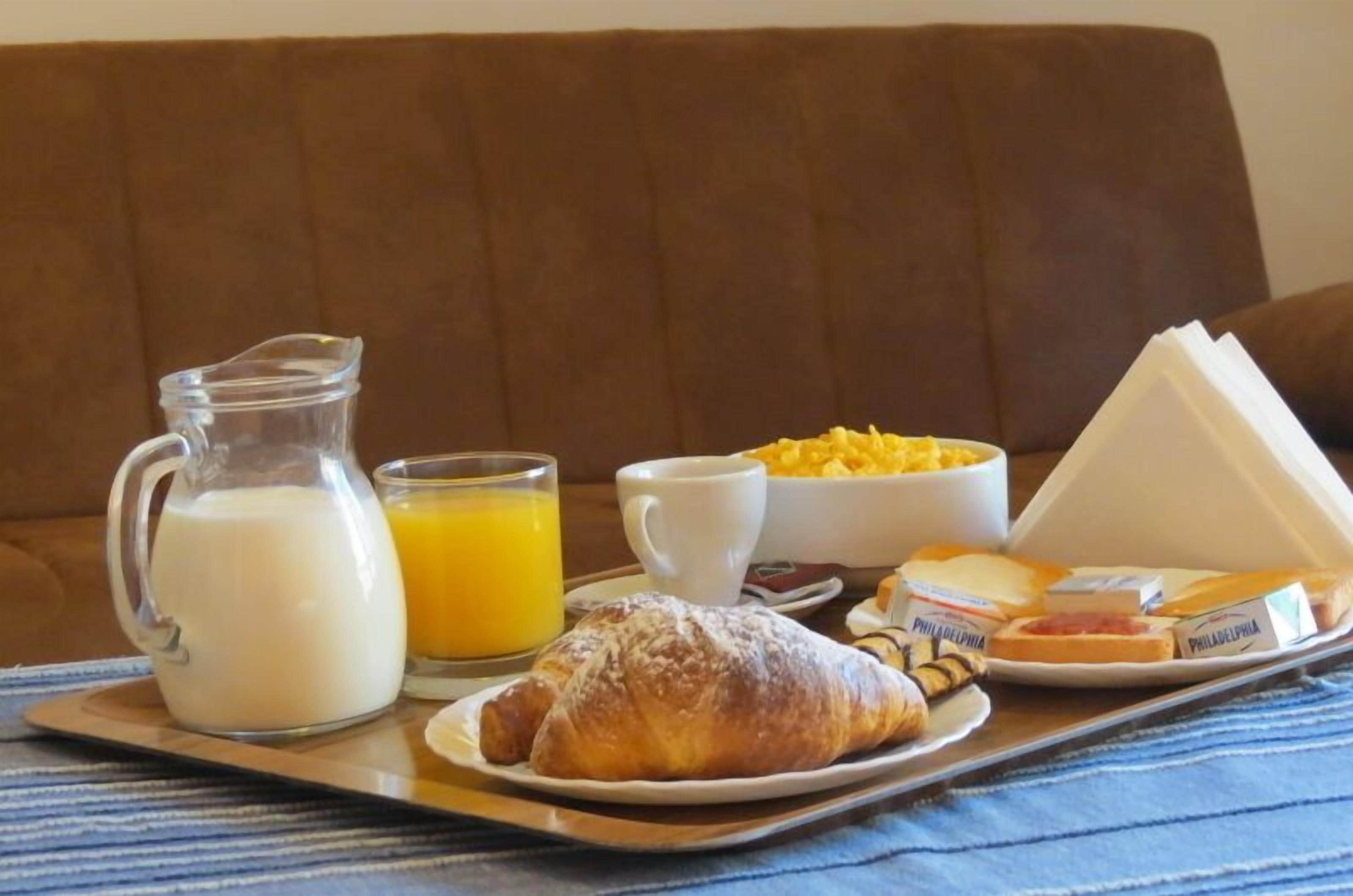 A breakfast tray with milk, orange juice, croissant, cheese, and bread on a tray.