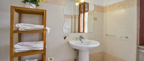 Un baño con un estante de madera con toallas, un lavamanos blanco y un espejo con luces arriba.