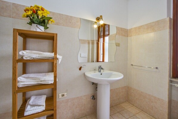 Un baño con un estante de madera con toallas, un lavamanos blanco y un espejo con luces arriba.