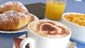 Un desayuno con cruasanes, una taza de café con arte latte, un vaso de jugo de naranja y un tazón de cereal.