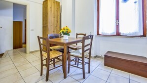 Un área de comedor con una mesa y sillas de madera, un florero con flores y una ventana con persianas.