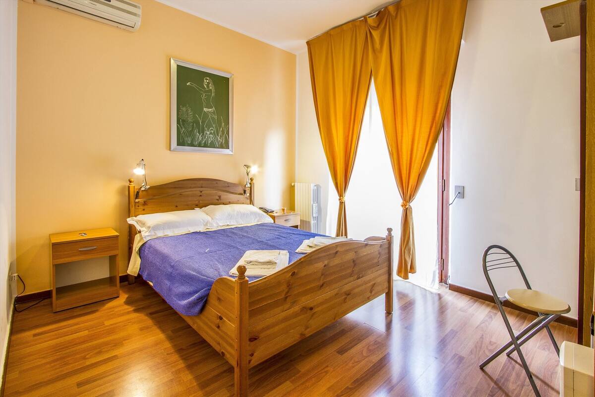 Ein Schlafzimmer mit einem hölzernen Bett, einem Nachttisch, einem Sessel und einem Fenster mit Vorhängen.