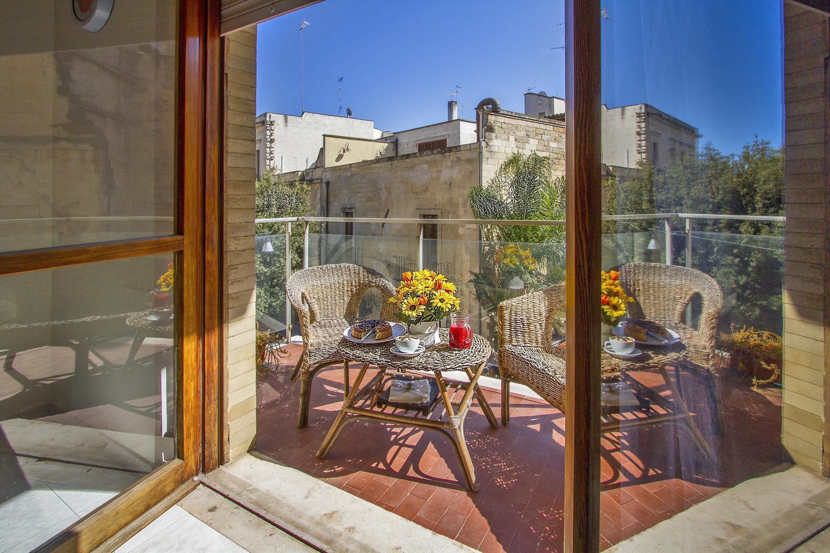 A balcony with wicker furniture, a table with a vase of flowers, and a view of buildings and trees.