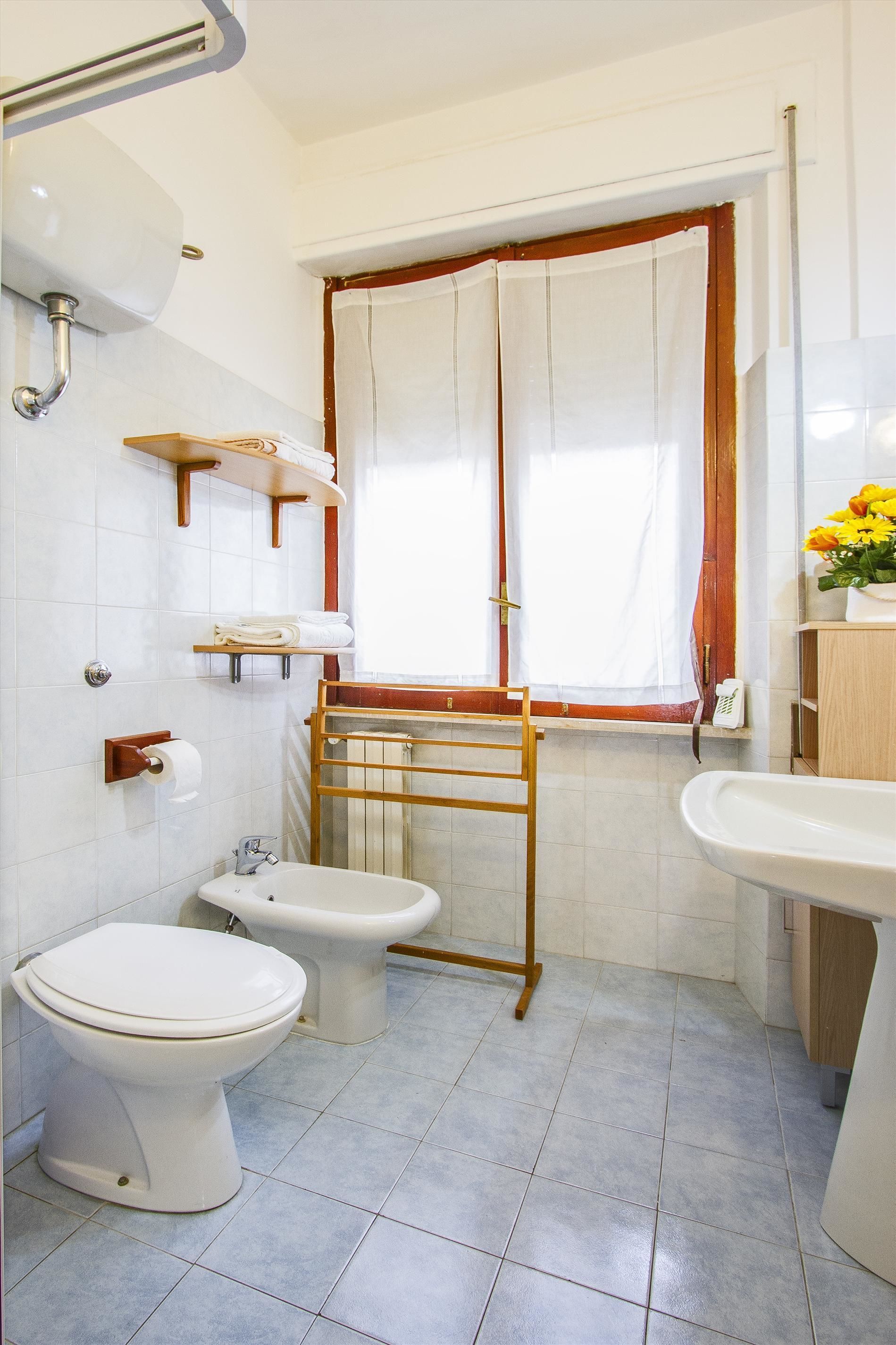 A bathroom with a toilet, bidet, and sink, a window with curtains, and a towel rack.
