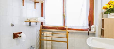 A bathroom with a toilet, bidet, and sink, a window with curtains, and a towel rack.
