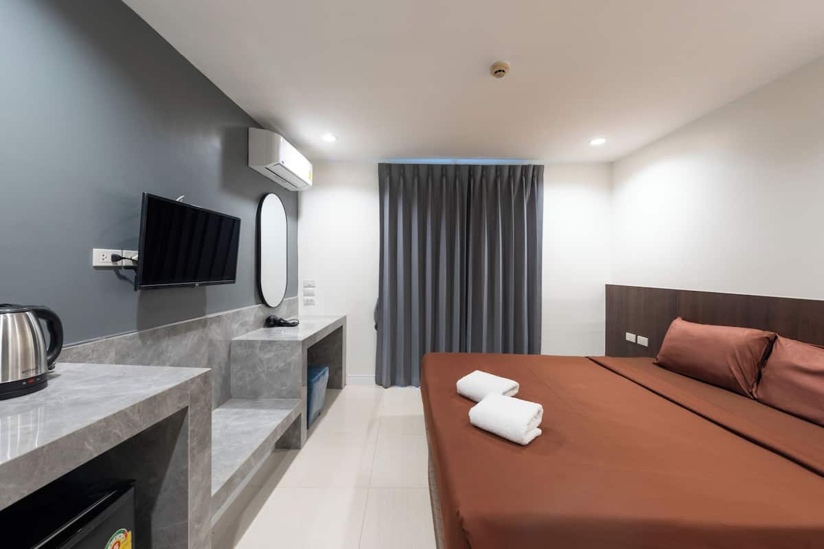 A modern hotel room with a bed, a desk with a kettle, a flat-screen TV, and a window with curtains.