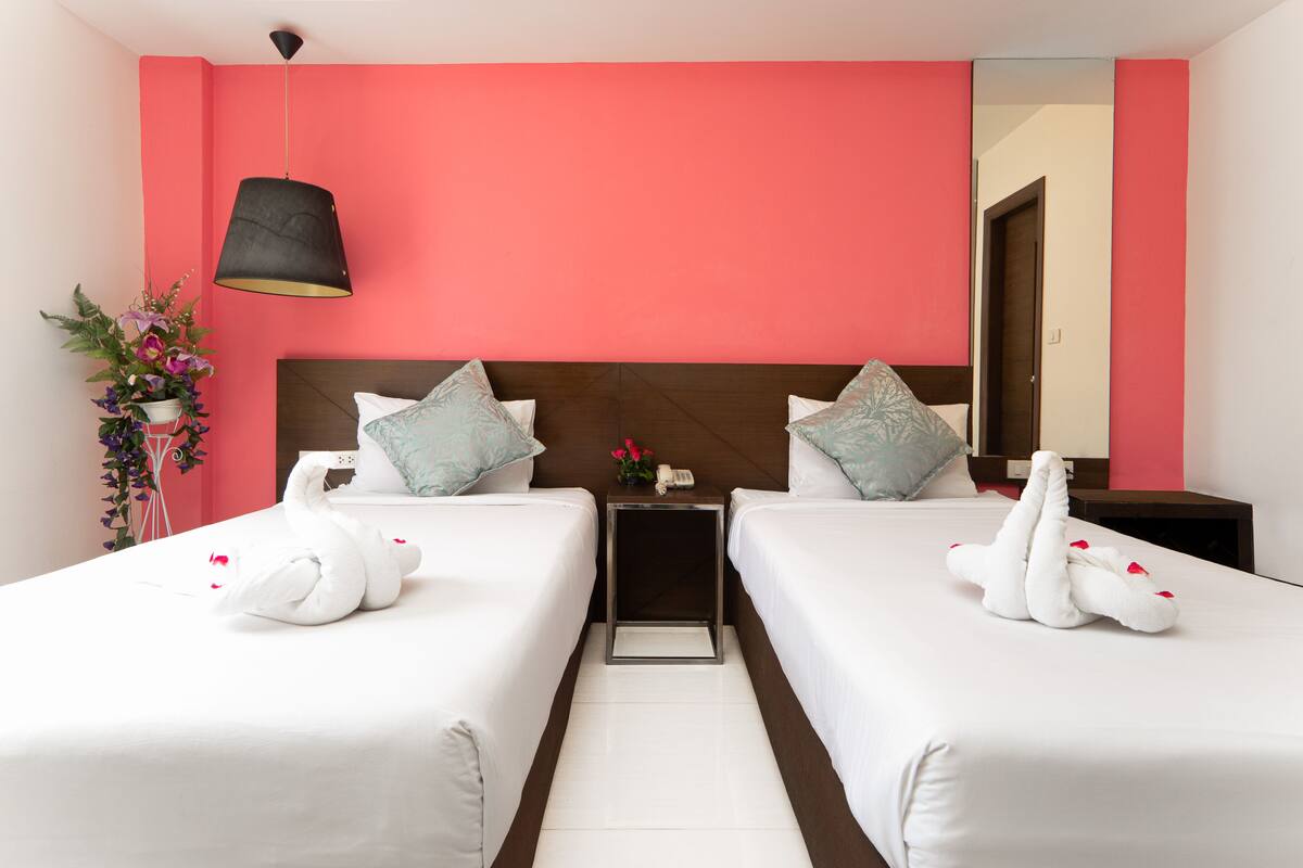 A hotel room with two beds, a nightstand, a lamp, and a mirror.