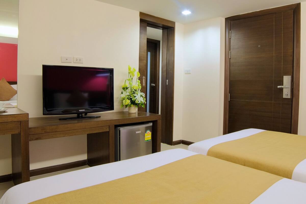 A hotel room with a bed, a TV, a desk with a laptop, and a refrigerator.