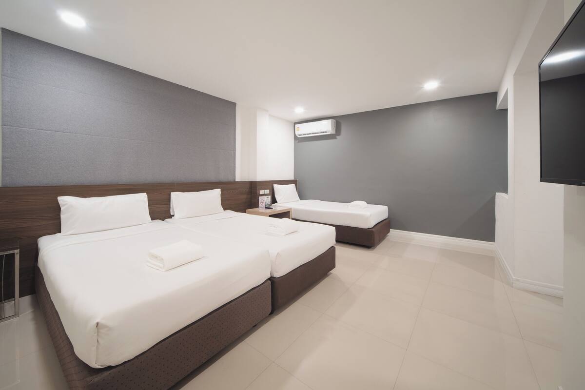 A modern hotel room with two beds, a flat-screen TV, and an air conditioning unit.