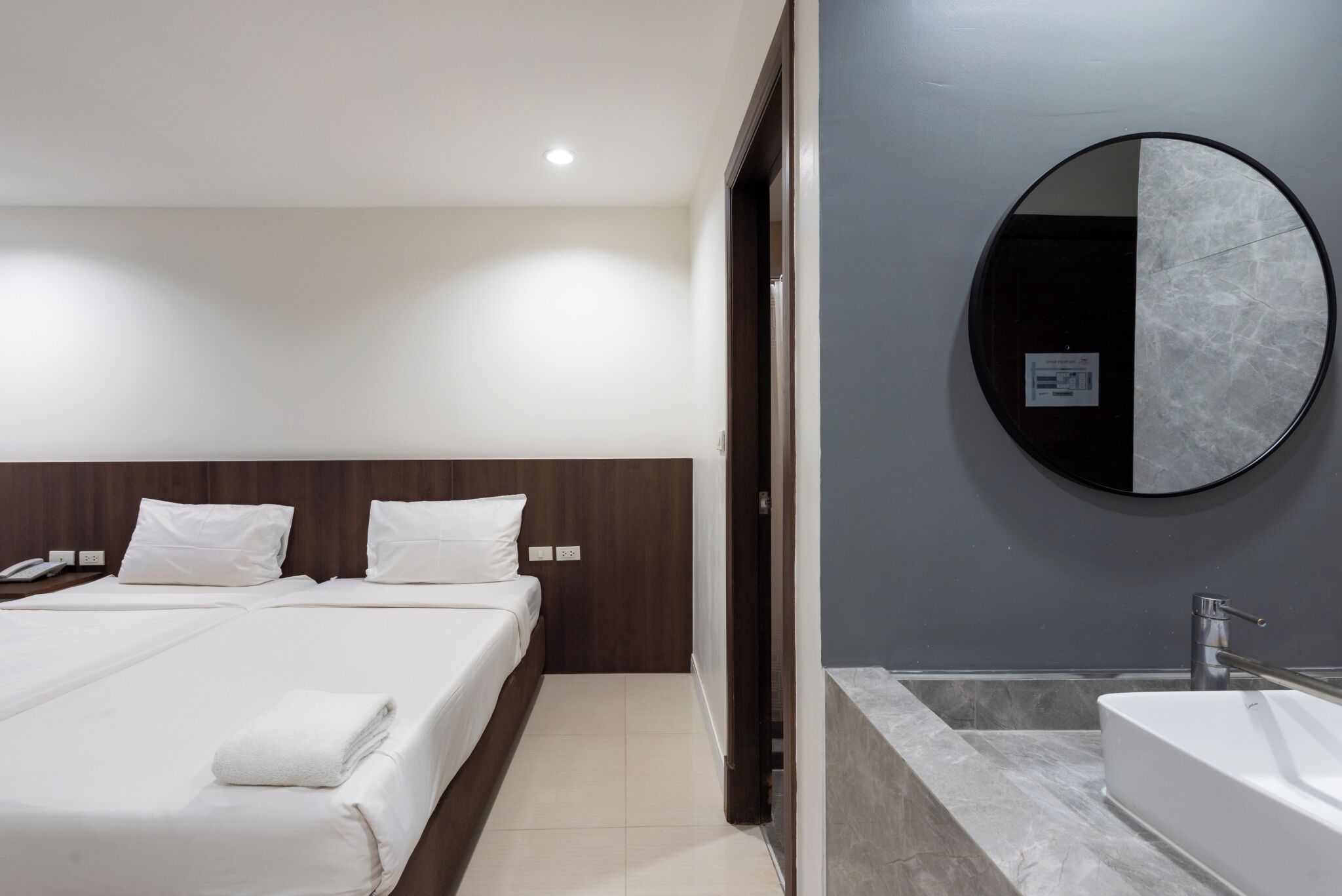 Une chambre d’hôtel moderne avec un grand lit, un miroir rond et une salle de bain séparée dotée d’une baignoire.