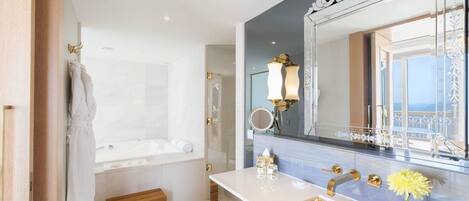 A modern bathroom with a large mirror, gold fixtures, and a view of the sea.