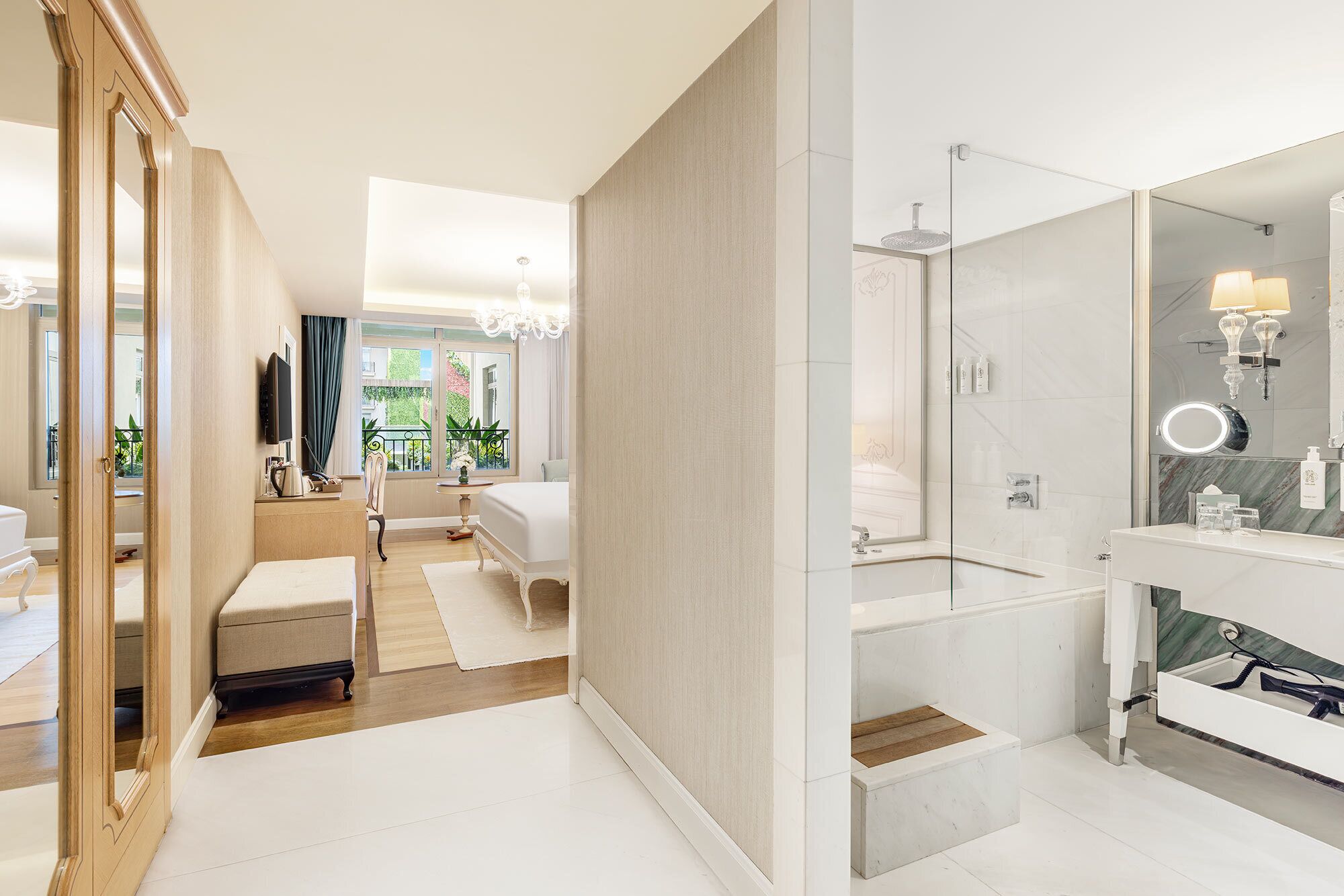 A modern hotel room with a large bed, a separate bathroom with a glass shower, and a view of the outdoors.