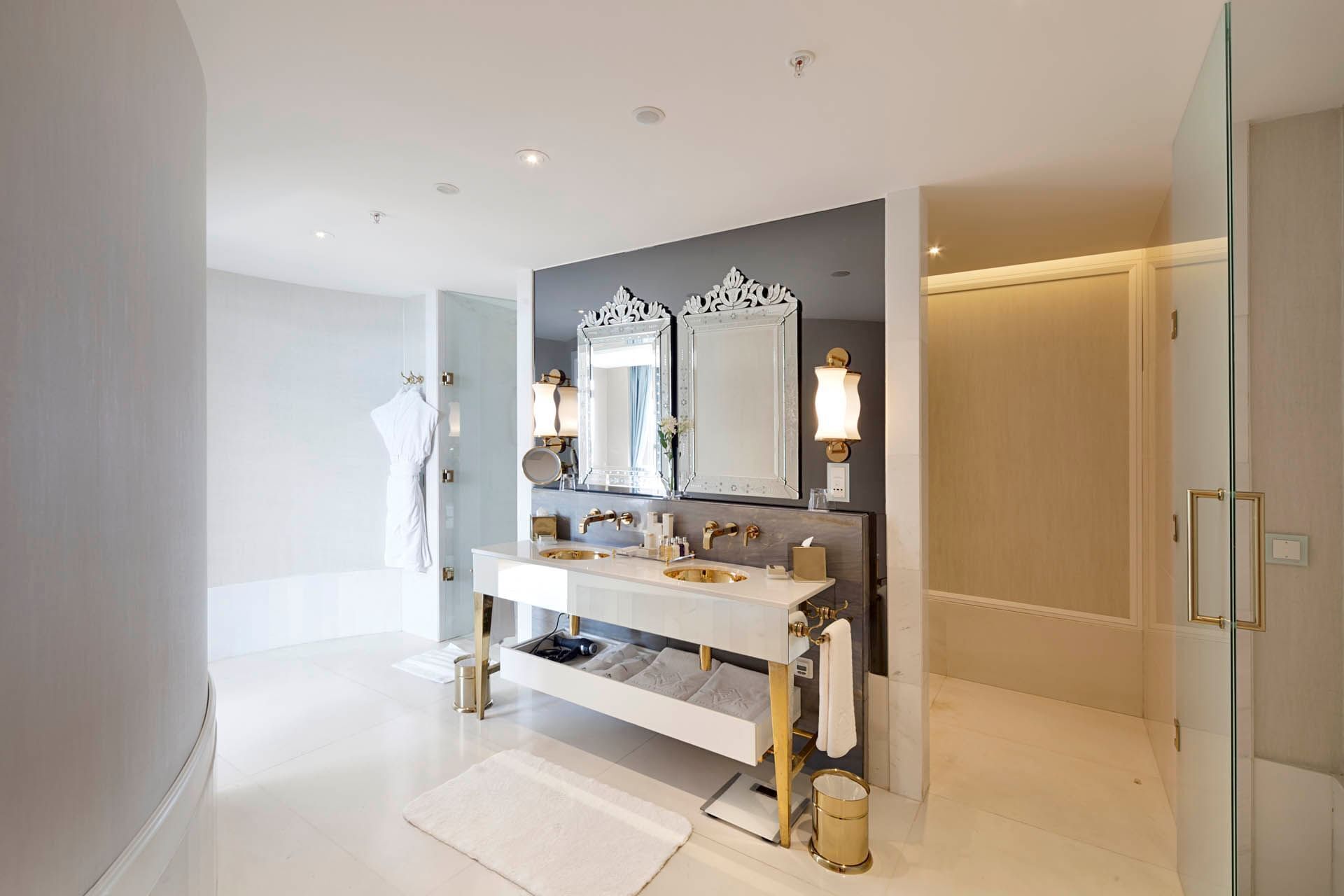 Une salle de bain moderne avec un grand meuble-lavabo, deux miroirs et un robinet doré.