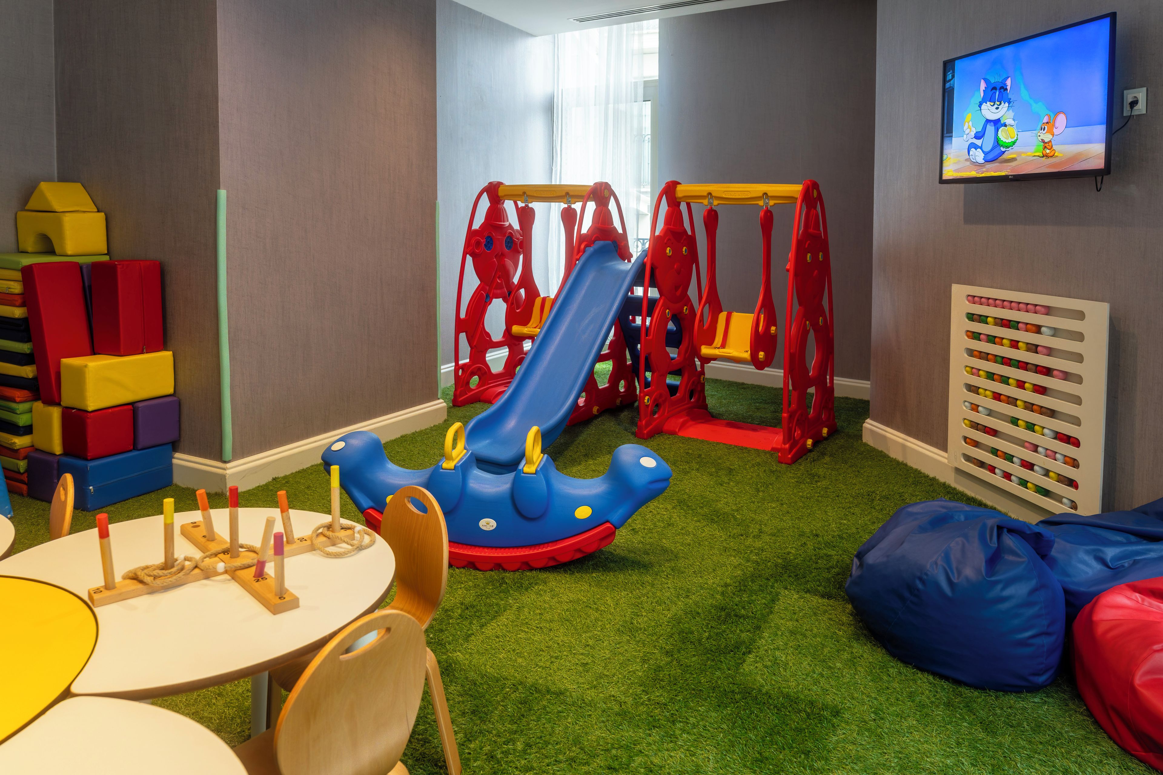 A children's play area with a slide, play structures, and a wall-mounted TV.