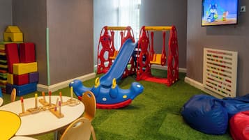 A children's play area with a slide, play structures, and a wall-mounted TV.