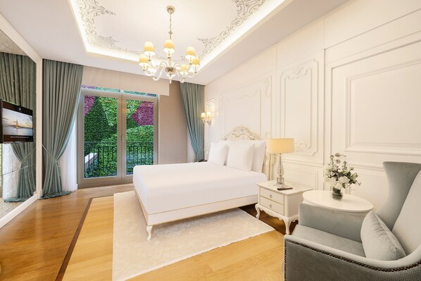 Une chambre avec un grand lit, une table de chevet, une chaise, un téléviseur et une vue sur la verdure grâce à une porte coulissante.