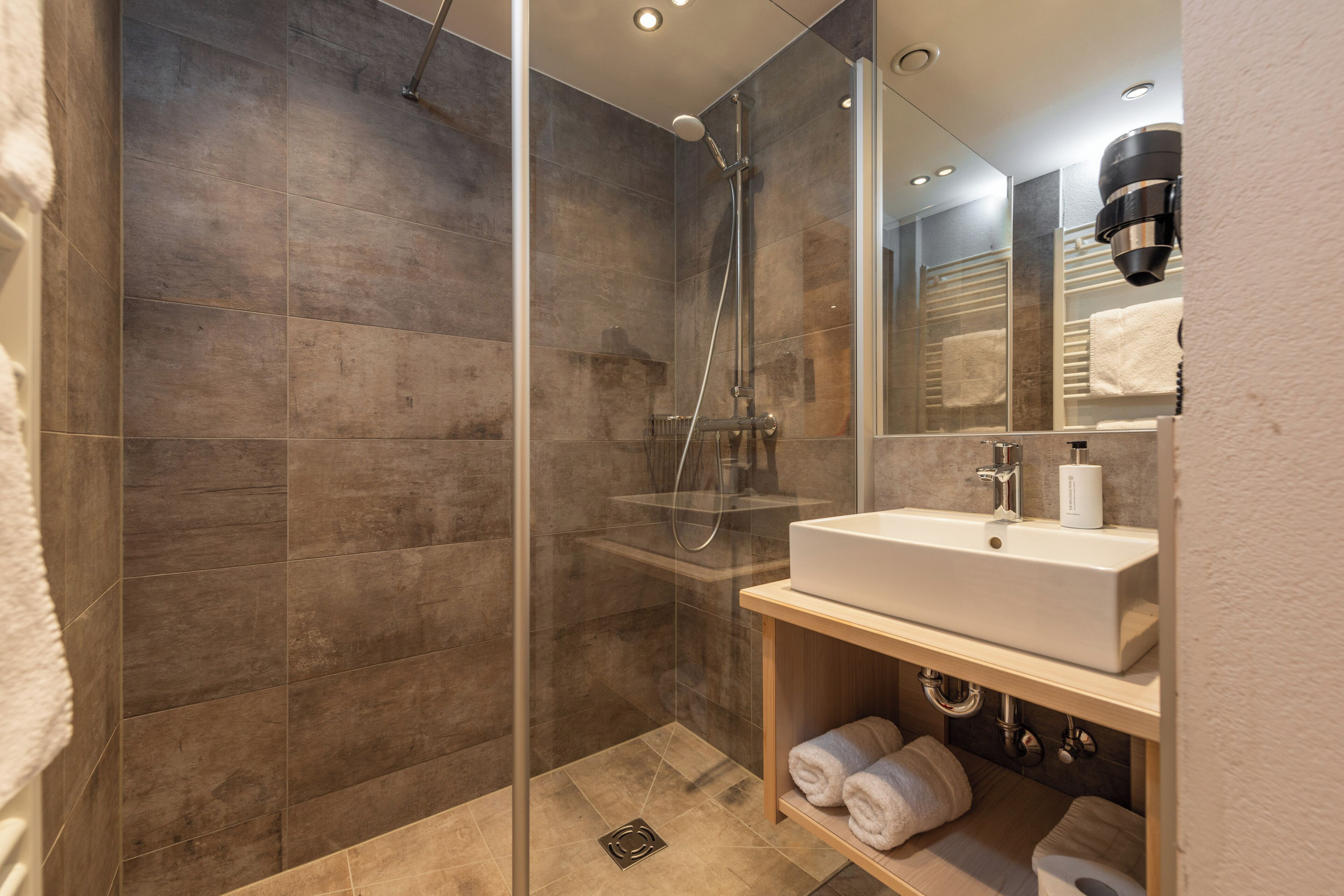 A modern bathroom with a glass-enclosed shower, a white sink, and a towel rack.