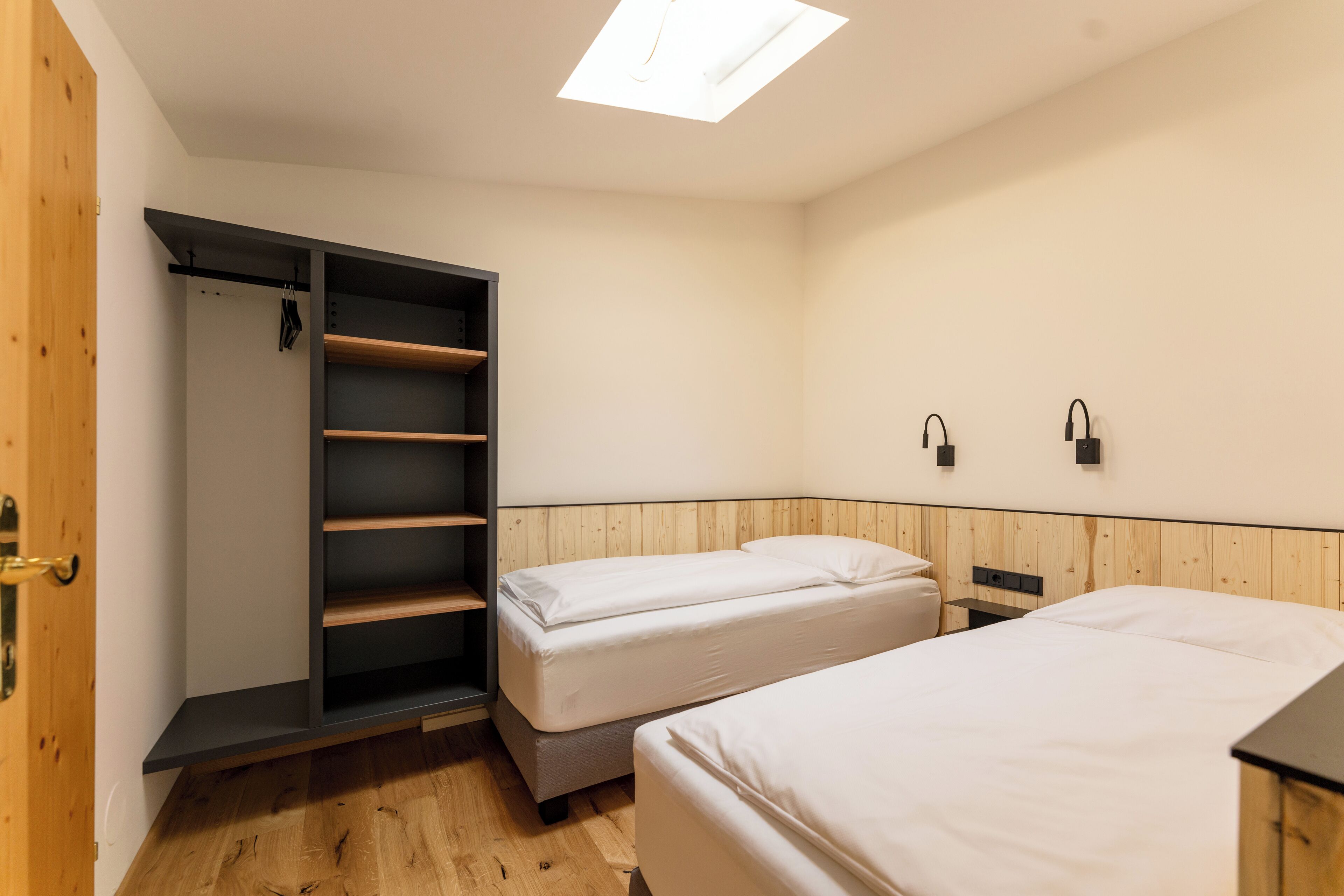 A room with two beds, a wardrobe, and a skylight.
