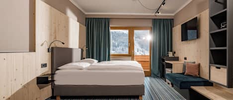 A modern hotel room with a large bed, a desk, a TV, and a view of a snowy landscape.